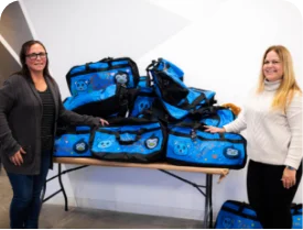 Two women standing on either side of a pile of completed Sweet Cases.