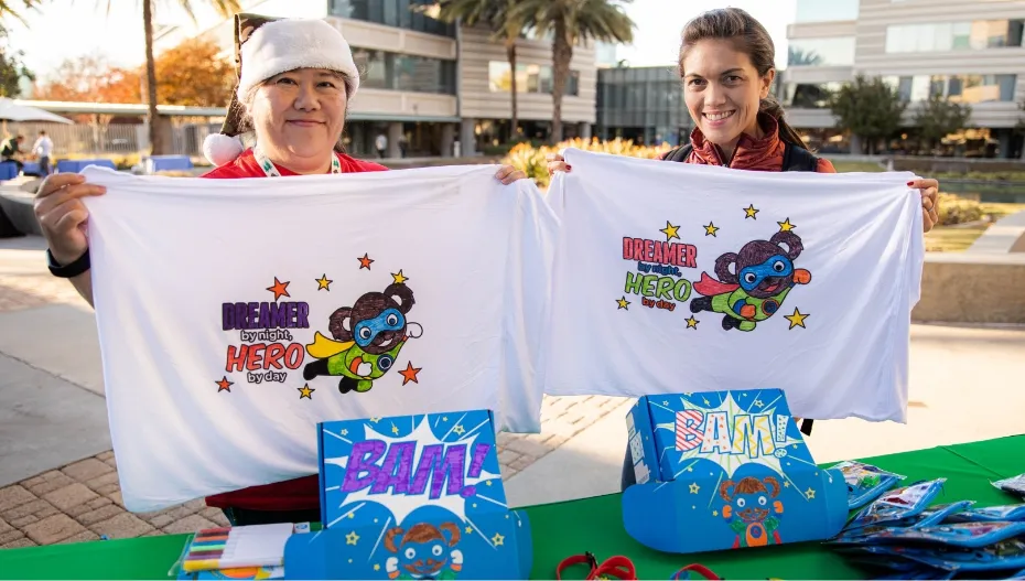 two volunteers holding up their decorated pillow cases from their superhero boxes