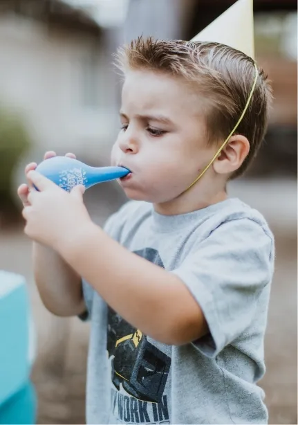 boy in birthday hat blowing a balloon