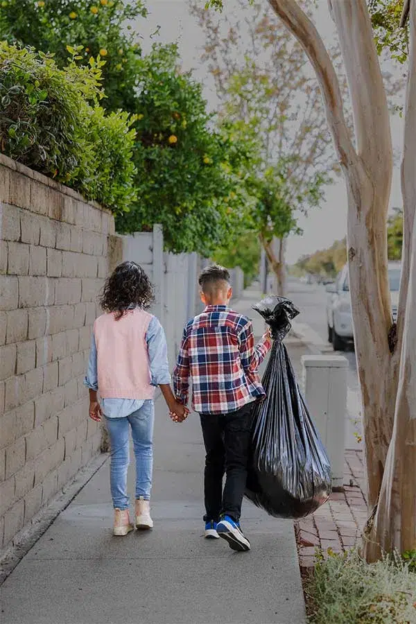 brother and sister siblings with trash bags walking down sidewalk
