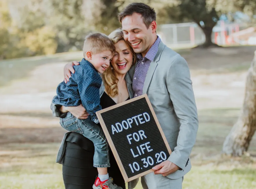 Family posing with an adoption sign that reads adopted for life