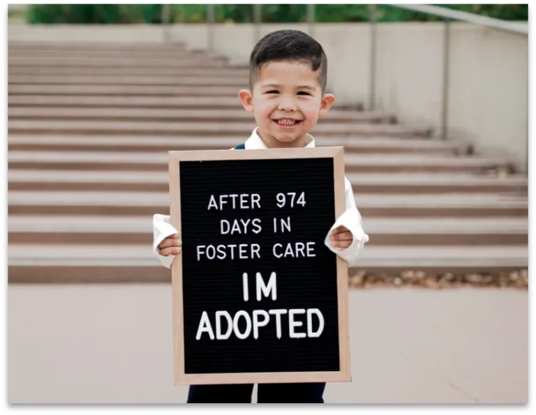 Little boy holding a sign that says After 974 Days in Foster Care I'm Adopted