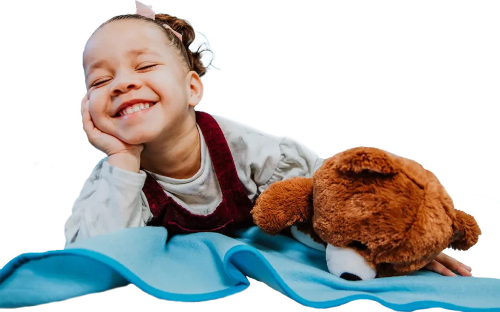 Girl smiling with her head on her chin next to her blanket and Foster Love teddy bear