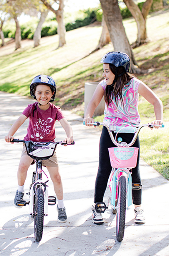 Two girls on bikes, wearing helmets in the park