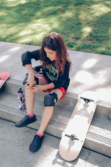 girl putting her knee pads on a street curb