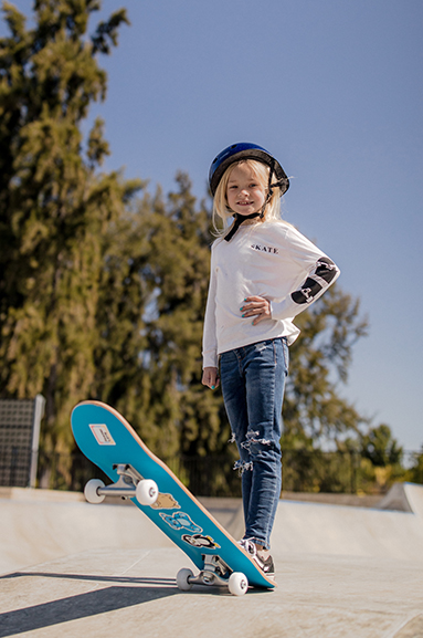 girl wearing safety gear posing with her skateboard, hand on her hip