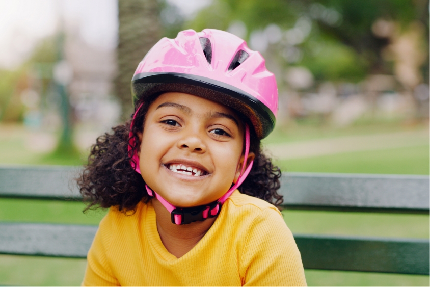 Girl in yellow on a park bench wearing her new pink bike helmet