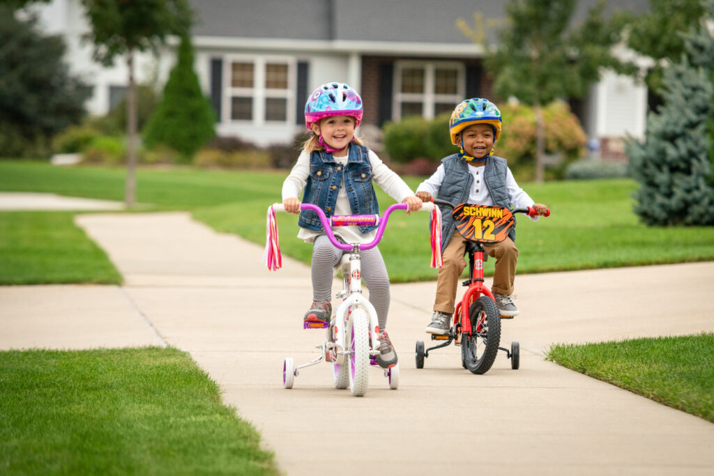Two children riding their bicycles down the sidewalk