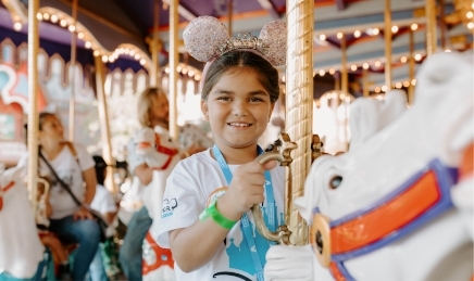Girl riding carousel wearing Mickey ears