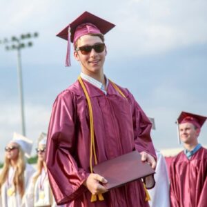 new graduate in maroon cap and gown wearing sunglasses holding a diploma