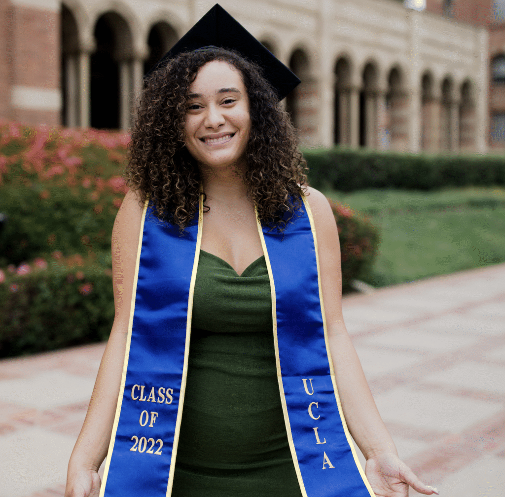 Foster Love Family Fellowship graduate in graduation cap and sash posing outside of university building.