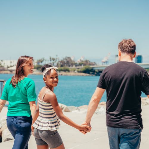 girl walking hand in hand with her parents looking back at camera